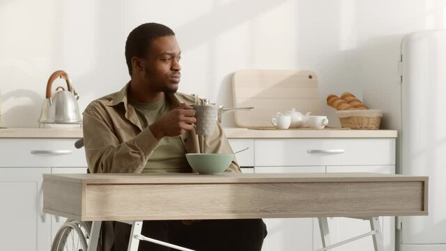 Thoughtful Disabled Black Man In Wheelchair Having Breakfast In Kitchen