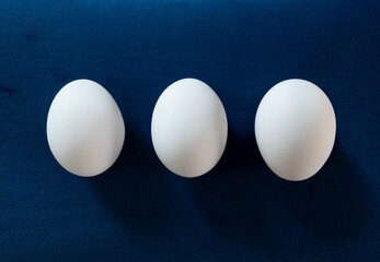 hilera de tres huevos blancos sobre fondo azul