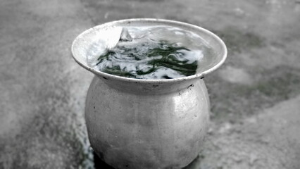 Close-up of glittering raindrops from A stainless steel Pot, with water flowing through the pot on a black and white for blurred background.