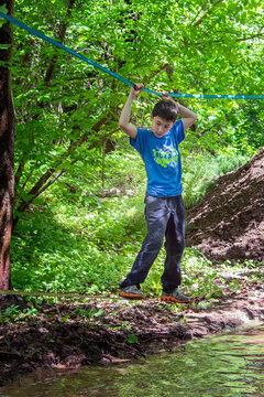 Young Boy Concentrating While Looking Down And Balancing On Ropes In A Fun Muddy Outdoor Obstacle Course In The Woods.