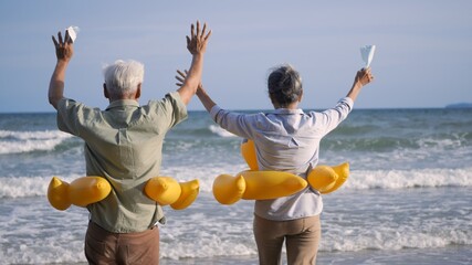 Happy senior couple wear rubber ring take off medical face mask and running to the beach enjoying life, relaxing after win coronavirus pandemic (COVID-19), plan life insurance at retirement couple