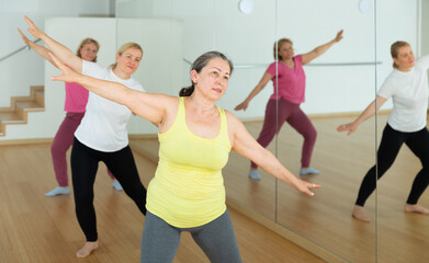 Naklejka na ściany i meble Active senior females doing stretching workout before group dance training
