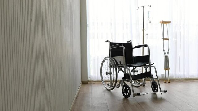 Zoom out technic video, wheelchair and crutches, walking aids with nobody in the room with a white curtain in the background. Disable people and health care concept.