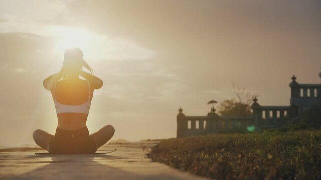 Behind woman on spiritual journey greeting bright sunlight in yoga lotus pose