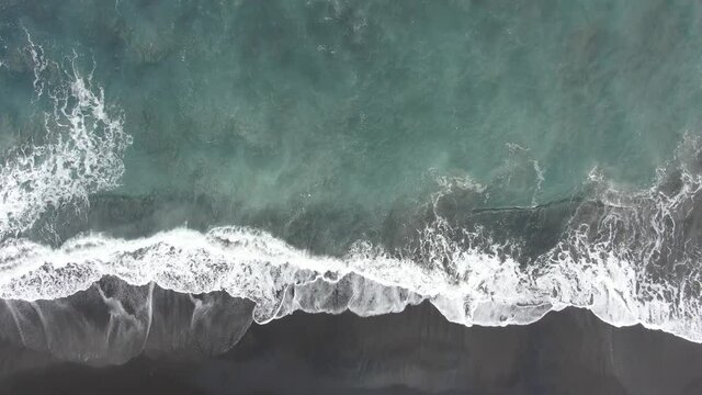 wave breaking on the shore on the black sand beach drone footage