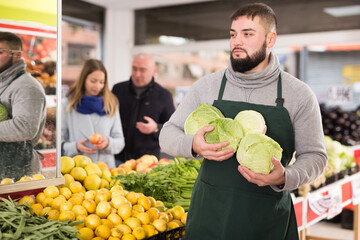 Male shop assistant lays fresh cabbage on counter in grocery shop. High quality photo