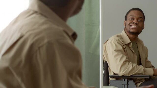 African guy in wheelchair looking at reflection in mirror indoor