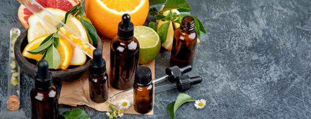 Bottles of essential aroma oils with citrus on dark gray background.