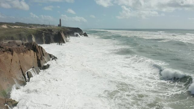 Flying past rocky coastline with white waves slamming onto cliffs