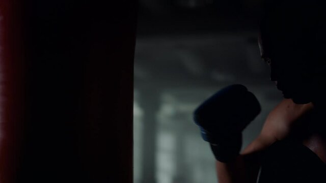 Athlete training boxing with punching bag. Man working out blows on sports bag