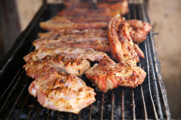 The pork is being grilled over charcoal.
