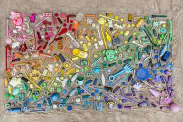 Colorful Plastics Found on the Beach Arranged into a Rainbow on a Sandy Beach Flat Lay Out