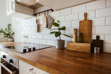 Kitchen brass utensils, chef accessories. Hanging kitchen with white tiles wall and wood tabletop.Green plant on kitchen background - 446544889