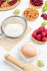 Flour in sieve, egg in small glass bowl. Tartlets with berries