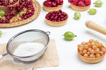 Flour in sieve and tartlets with berries.