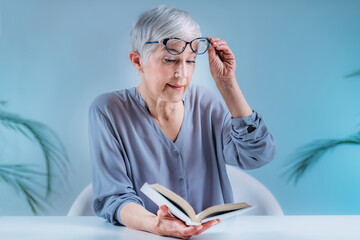 Senior Woman With Eyeglasses Having Problems with Book Reading. Indication for Cataract, Glaucoma, and Vision Loss in the Elderly. - obrazy, fototapety, plakaty