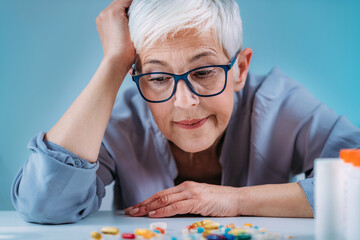 Medicine non adherence. Senior woman looking pills, not sure if she had taken the medicine or not - obrazy, fototapety, plakaty