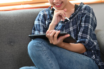 Cropped shot smiling young female sitting on couch and using digital tablet.