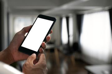 Close up view man holding mock up mobile phone woh empty screen in living room.