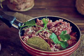 A frying pan with stewed meat seasoned with fresh herbs on a wooden countertop.