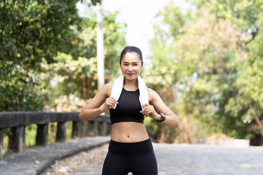 Smiling asian woman wearing black sportswear and sweat wipes on neck and exercising outdoor. Healthy and sport concept.