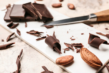 Board with chocolate curls, nuts and knife on grunge background