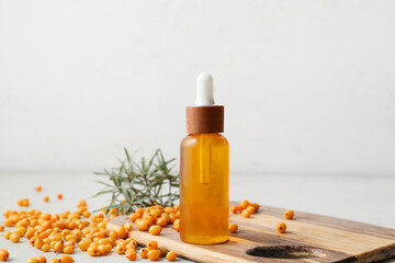 Bottle of sea buckthorn essential oil on light background
