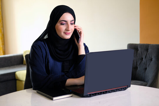 Arab working remotely from home. Emirati national at work. Woman wearing Abaya Hijab