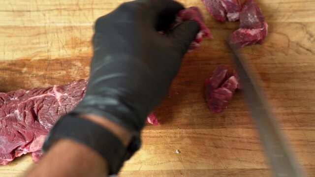 Chef is dicing the most delicious fresh chuck of beef, using black gloves and sharp chef knife. (close up shot - top view)