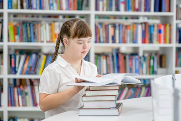 Smart young girl with syndrome down reads a book at library. Education for disabled children concept