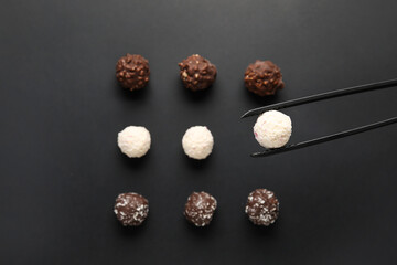 Tongs with sweet chocolate candies on dark background
