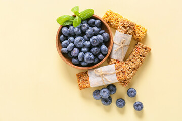 Healthy cereal bars and blueberries on color background