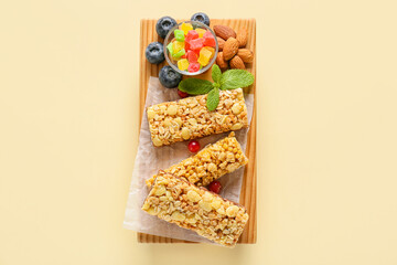 Board with healthy cereal bars, berries and nuts on color background
