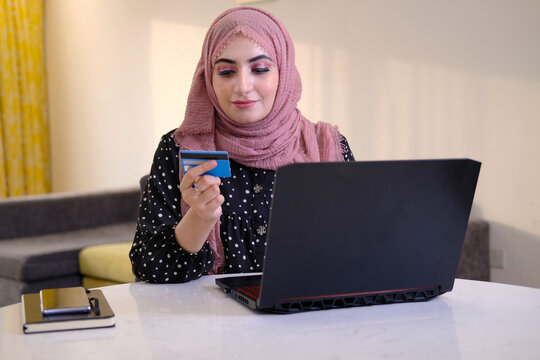 Online Buying Concept Of A Arabic Woman Wearing Head Scarf As Part Of Traditional Custome Using Mobile Cell Phone.  Emirati Lady Using Mobile Device Browsing The Internet Or Doing Online Banking