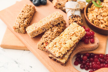 Board with healthy cereal bars and berries on light background