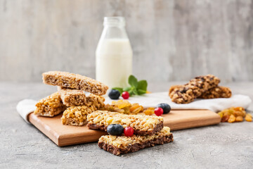 Board with healthy cereal bars, berries and raisins on grey background
