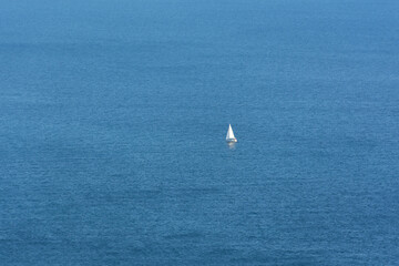 Fototapeta premium White sailboat sea. The endless blue sea, the concept of minimalism, loneliness, summer relaxation. A lone white boat is traveling in the ocean. Sea tourism, towards adventure. Top view, copy space