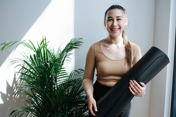 Happy young woman with genuine smile posing with a yoga mat, hugging it.