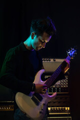 Handsome young male musician with electric guitar in recording studio. Rock musician performance in dark background with light neon effect.