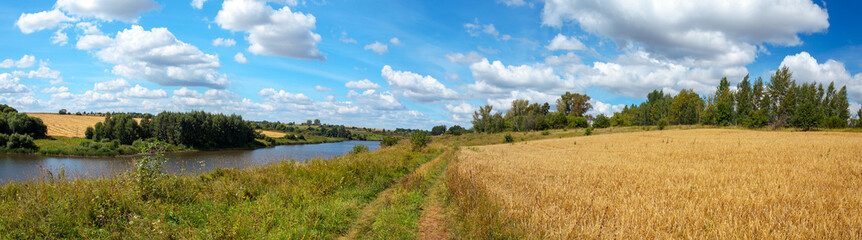 Obraz na płótnie Canvas Summertime scenery.Beautiful rural view of blue sky over the calm river and golden wheat fields during sunny summer day.Summer countryside panorama.