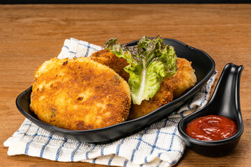 High angle view of delicious homemade croquette in black plate on table cloth with ketchup in black cup.