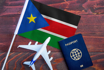 Flag of South Sudan with passport and toy airplane on wooden background. Flight travel concept
