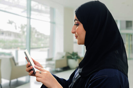 Close up of Arab woman browsing on her mobile cellular phone wearing a traditional Emirati Hijab and black Abaya in the Middle East Gulf