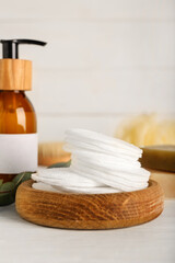 Holder with cotton pads and bottle of cosmetic product on light background, closeup
