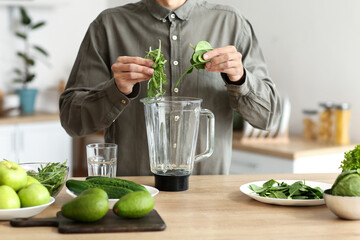 Young man preparing healthy green smoothie in kitchen