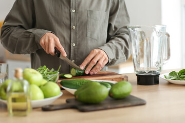 Young man cutting cucumber in kitchen
