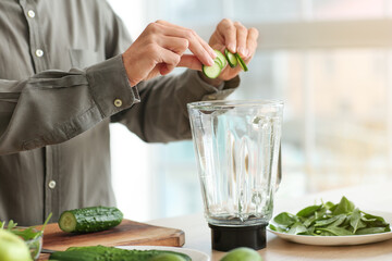 Young man preparing healthy green smoothie in kitchen