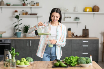 Young woman pouring healthy green smoothie into glass in kitchen