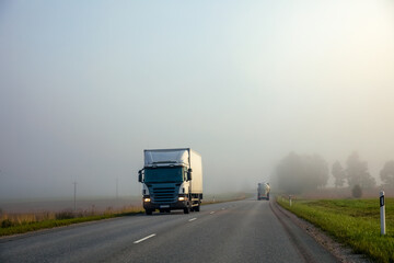 Truck on a country road in the fog in summer. Poor visibility conditions on the road.