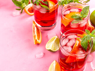 Refreshing summer red cocktail in glasses with blood orange and lime on pink background with mint